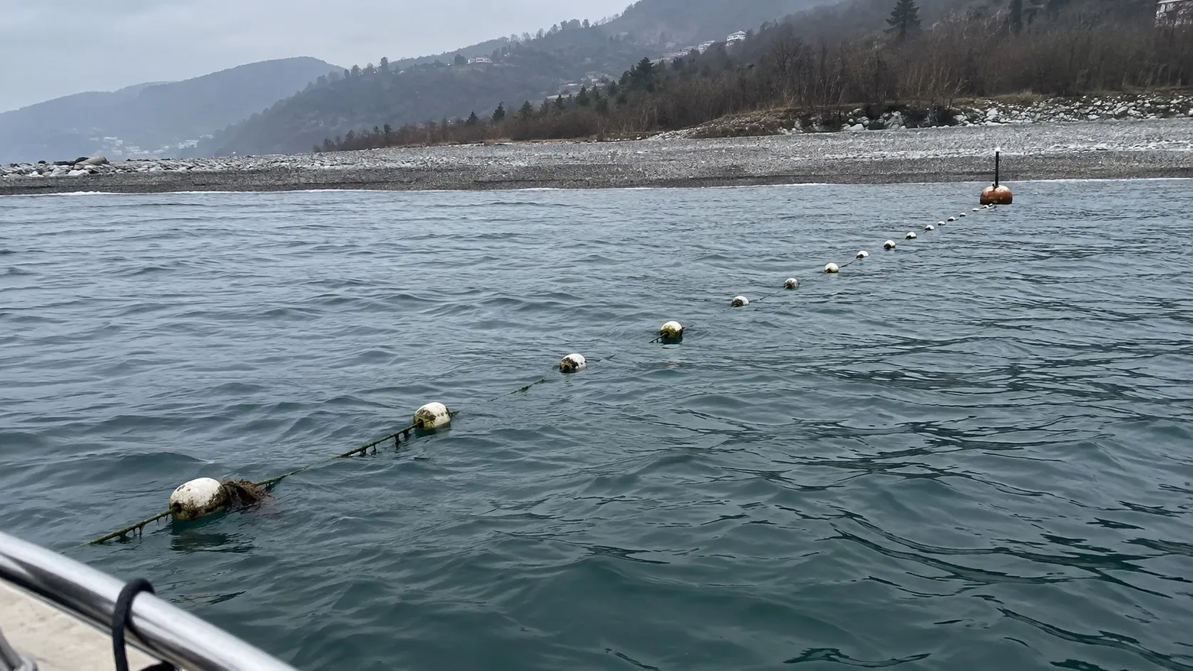 Цепочка поплавков ставной сети на тихой февральской воде у каменистого берега — сама сеть уходит в глубину