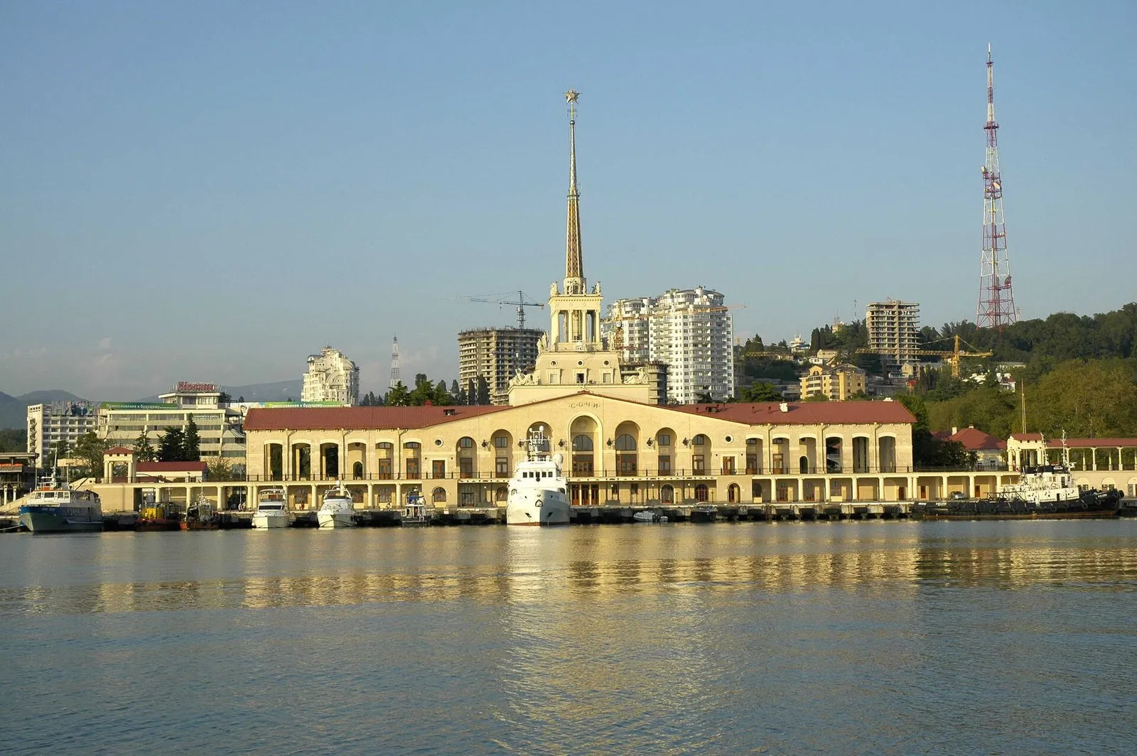 Морской вокзал из гавани, май 2009 года: шпиль над причалами, а правее, на склоне, — красно-белая решётчатая мачта телебашни (фото: Ганощенко Роман (Ganoshenko Roman), Wikimedia Commons, CC BY-SA 3.0)