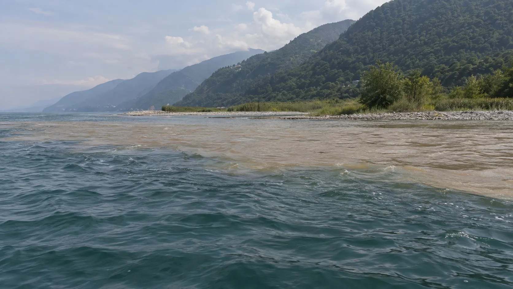 Устье реки у низкого берега: пресная вода мутной полосой вливается в море