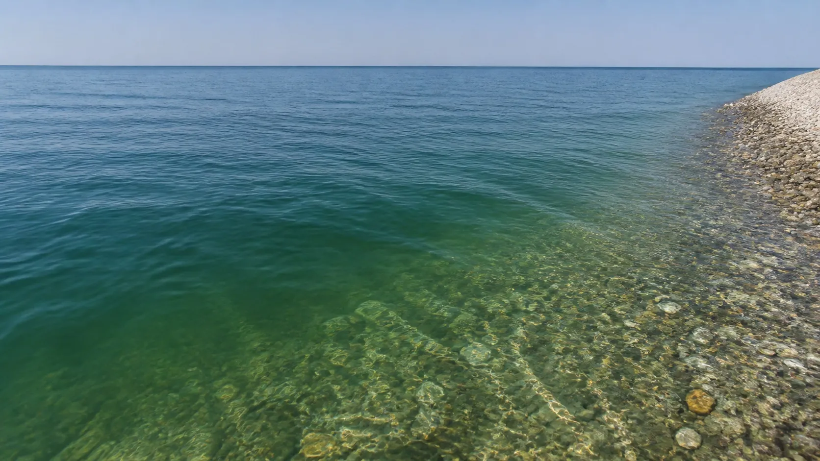 Прозрачная вода у самого берега: дно читается первые метры, дальше уходит в зелёную муть. Мелководье и есть причина, по которой борт держится мористее