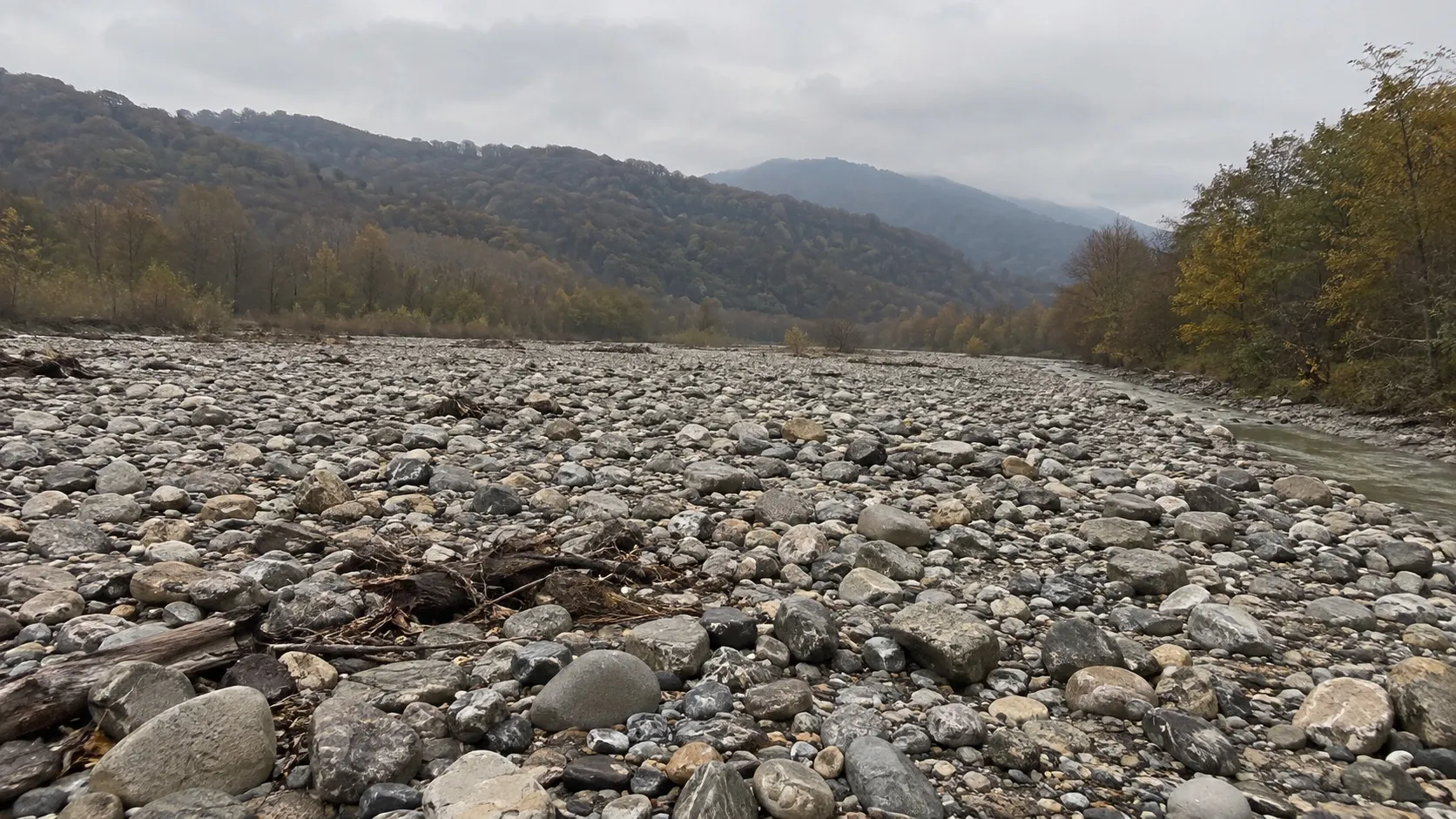 Галечное русло горной реки в межень: окатанные камни и узкая протока серо-зелёной воды (иллюстрация)