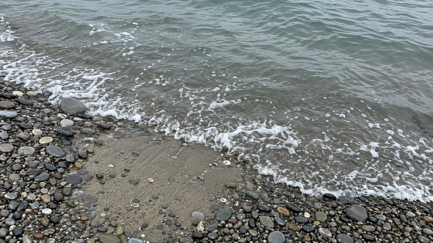 Иллюстрация: песчаное пятно среди гальки у кромки воды