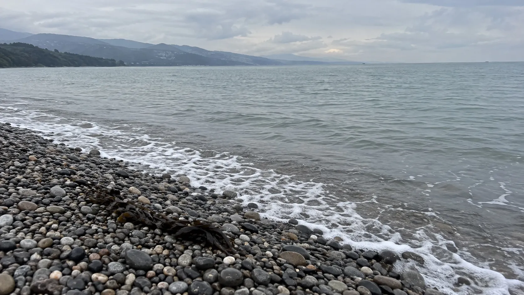 Мокрая галька у кромки воды апрельским утром, серо-зелёная вода (иллюстрация, сгенерирована)