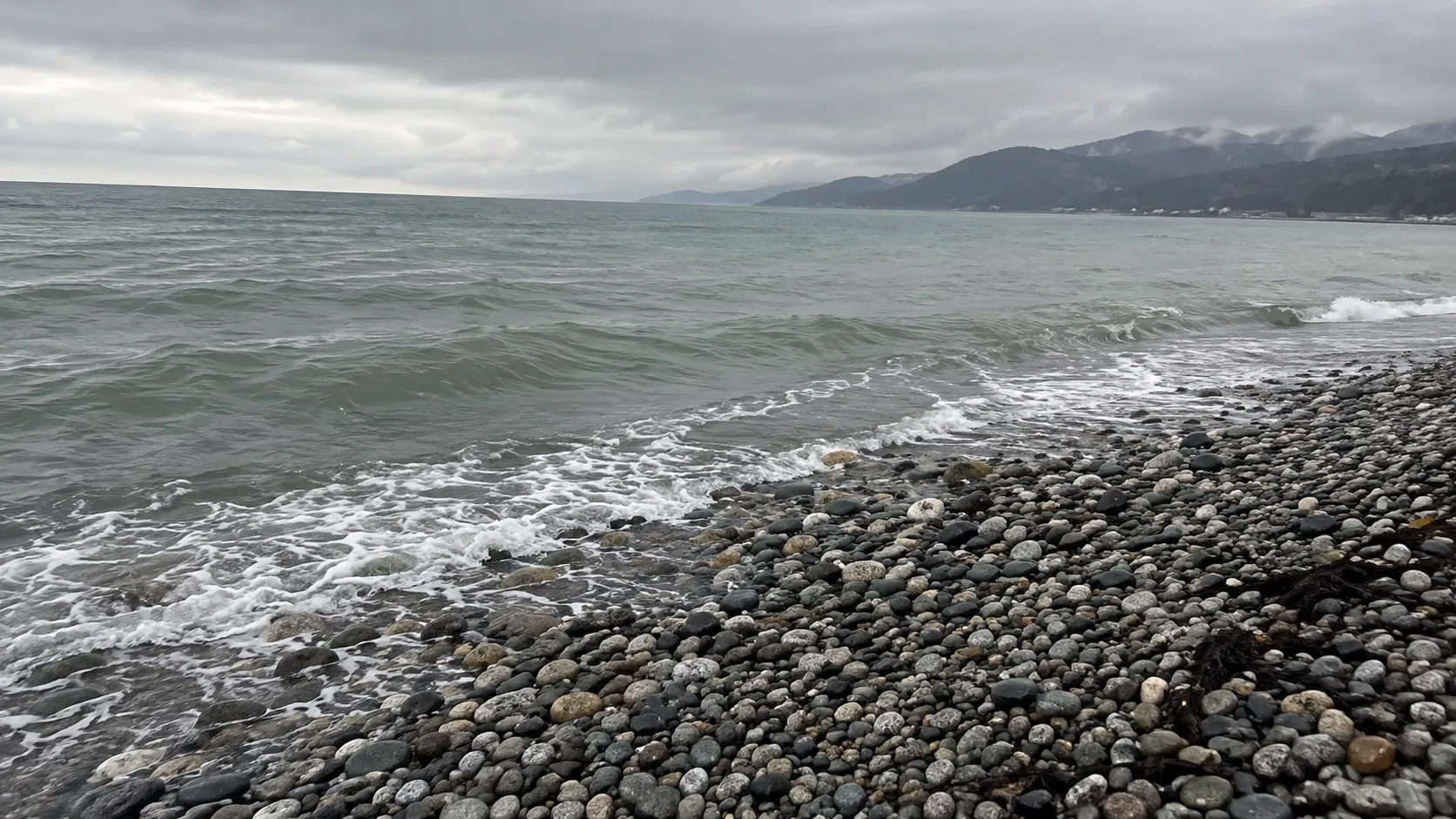 Мокрая галька у кромки воды в мартовскую морось, серо-зелёная вода