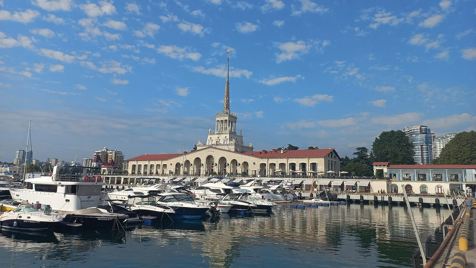 Яхты и катера у причалов Морского порта Сочи, за ними Морвокзал со шпилем, август 2022 года