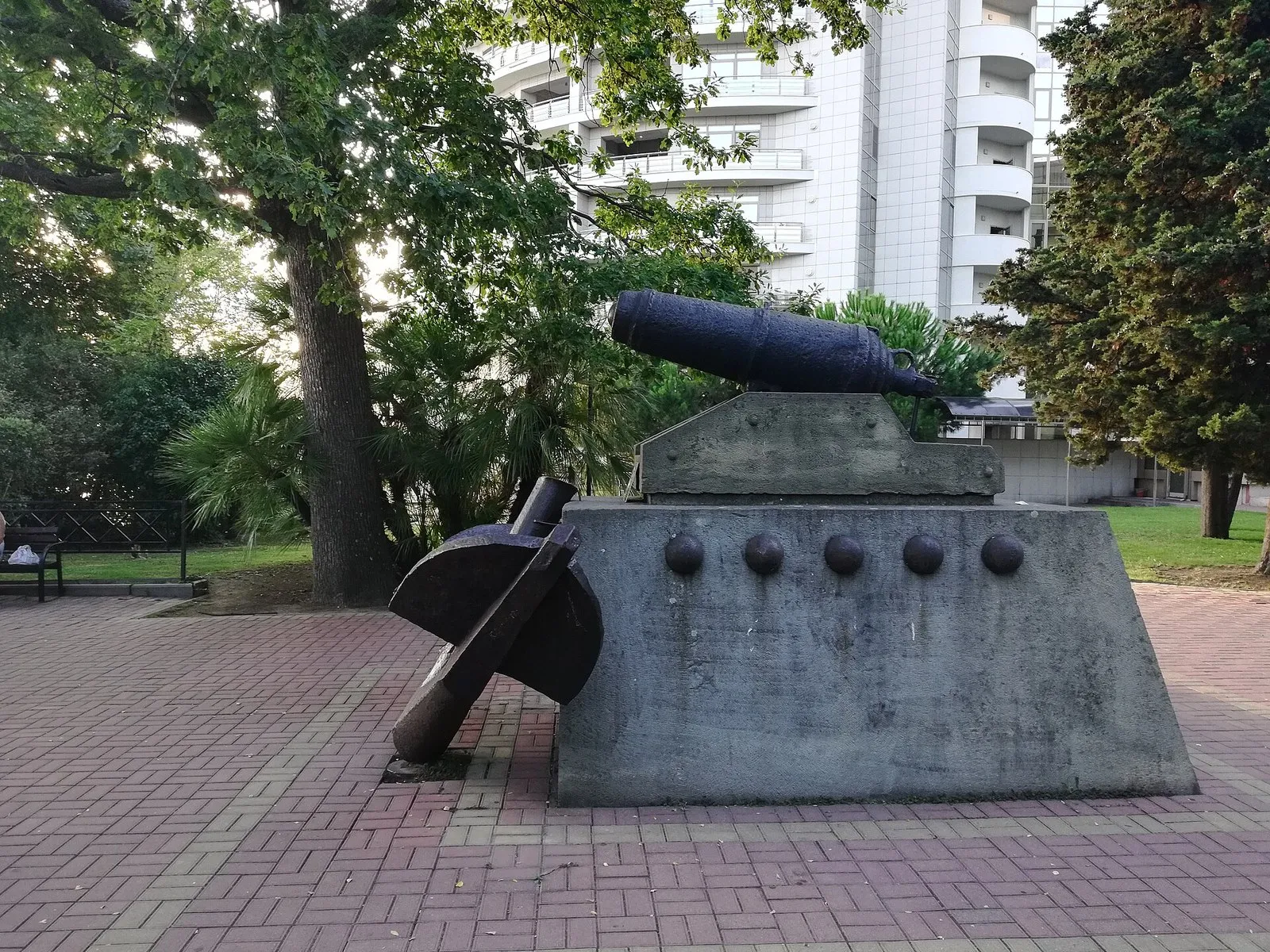 Корабельная пушка на лафете, ядра в нишах постамента, якорь у основания