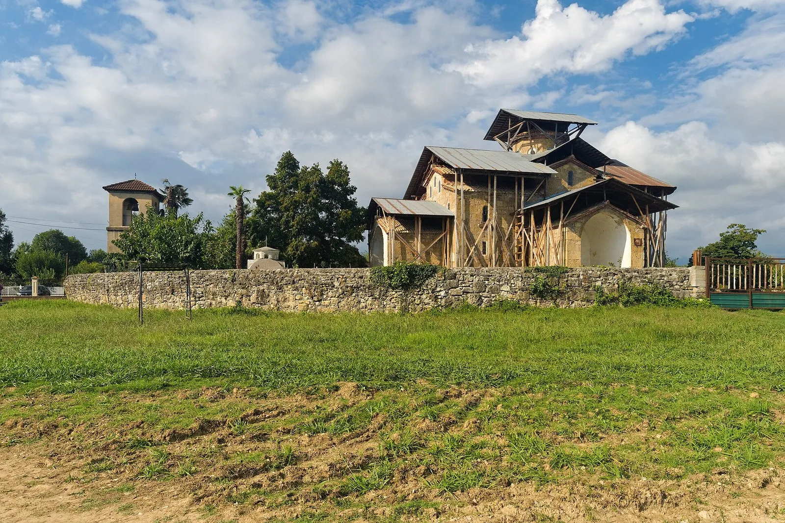 Храм Успения в Лыхны за каменной оградой, на стенах строительные леса