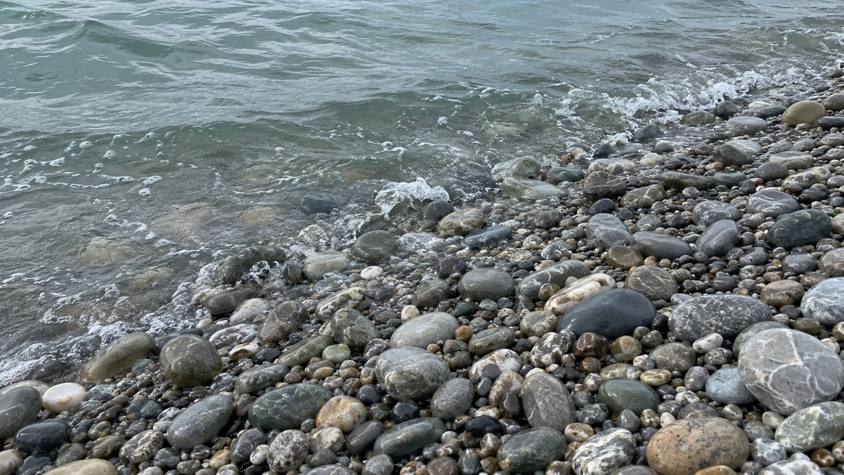 Мокрая галька у кромки серо-зелёной воды. Иллюстрация, созданная нейросетью