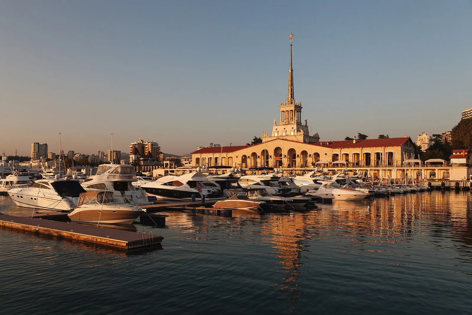Морской порт Сочи вечером: яхты и катера у причалов, шпиль Морского вокзала в закатном свете