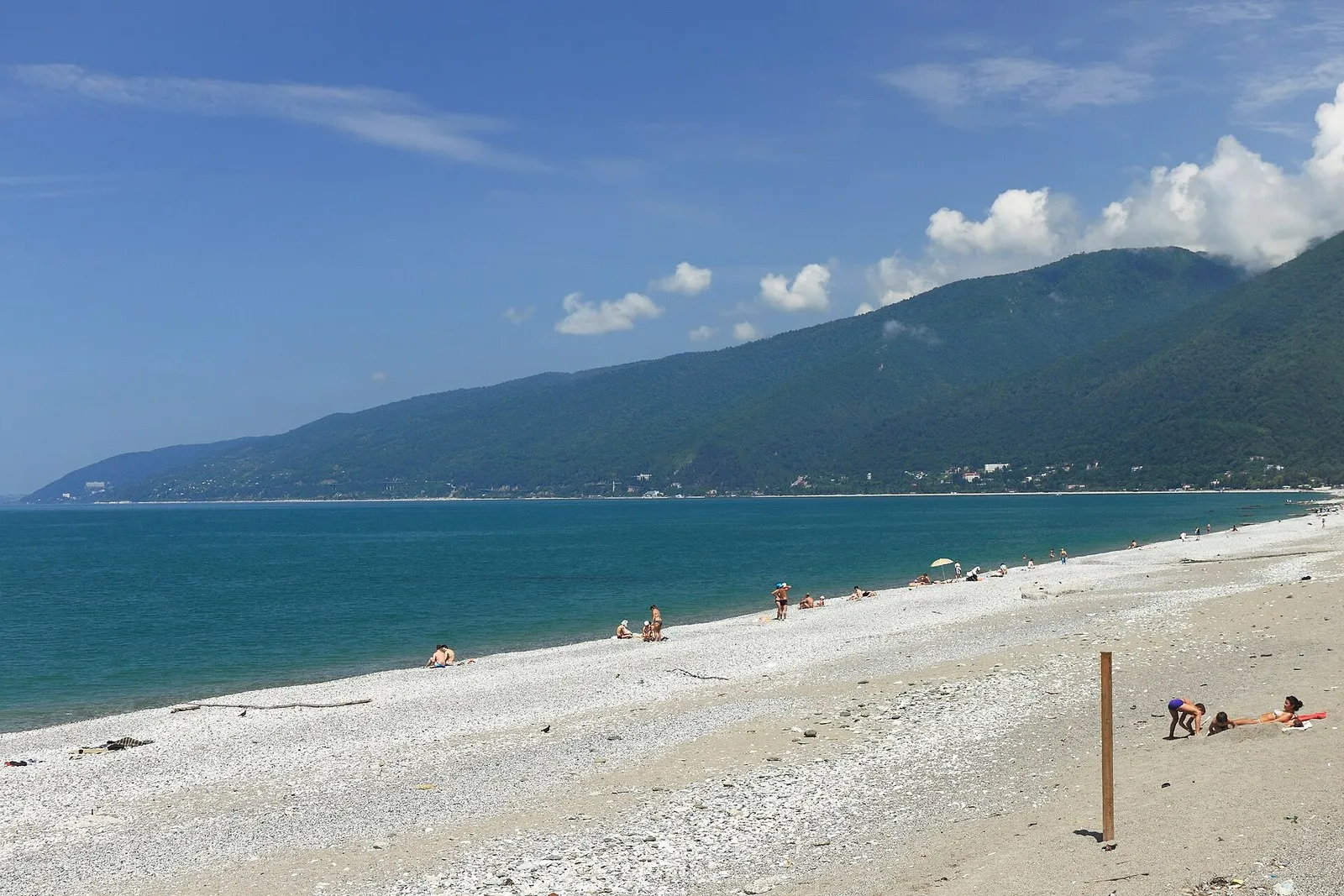 Галечный пляж в Гагре: полоса берега, море и лесистые горы над ним