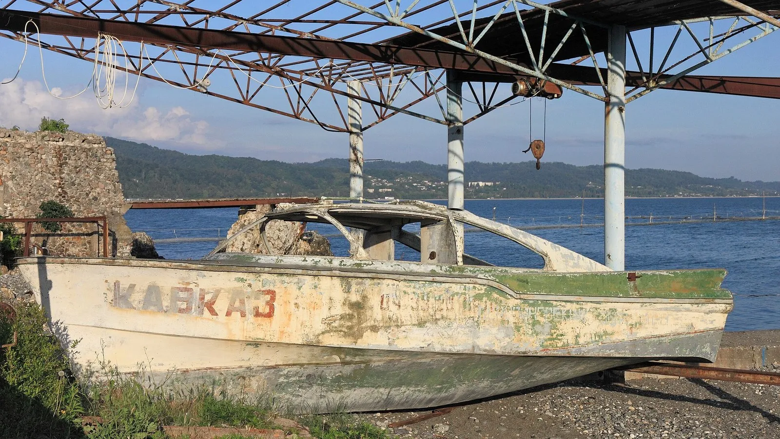 Старая моторная лодка с надписью «Кавказ» на берегу в Сухуме, за ней бухта