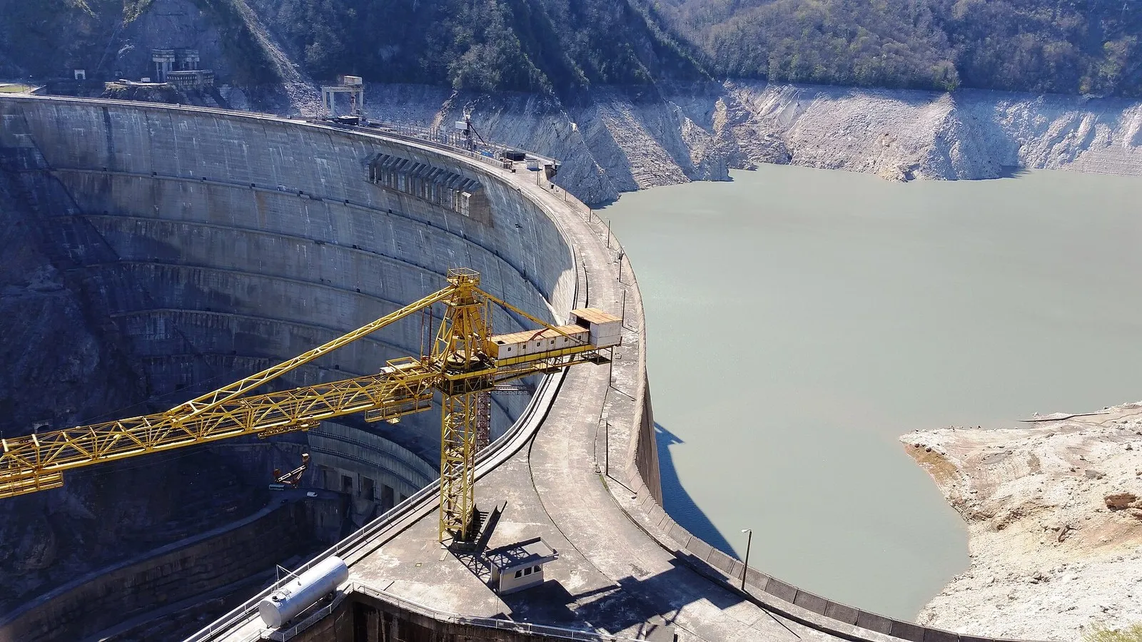 Плотина Ингурской ГЭС 5 апреля 2016 года: над серой водой водохранилища тянется светлая кайма голой породы, жёлтый кран на гребне