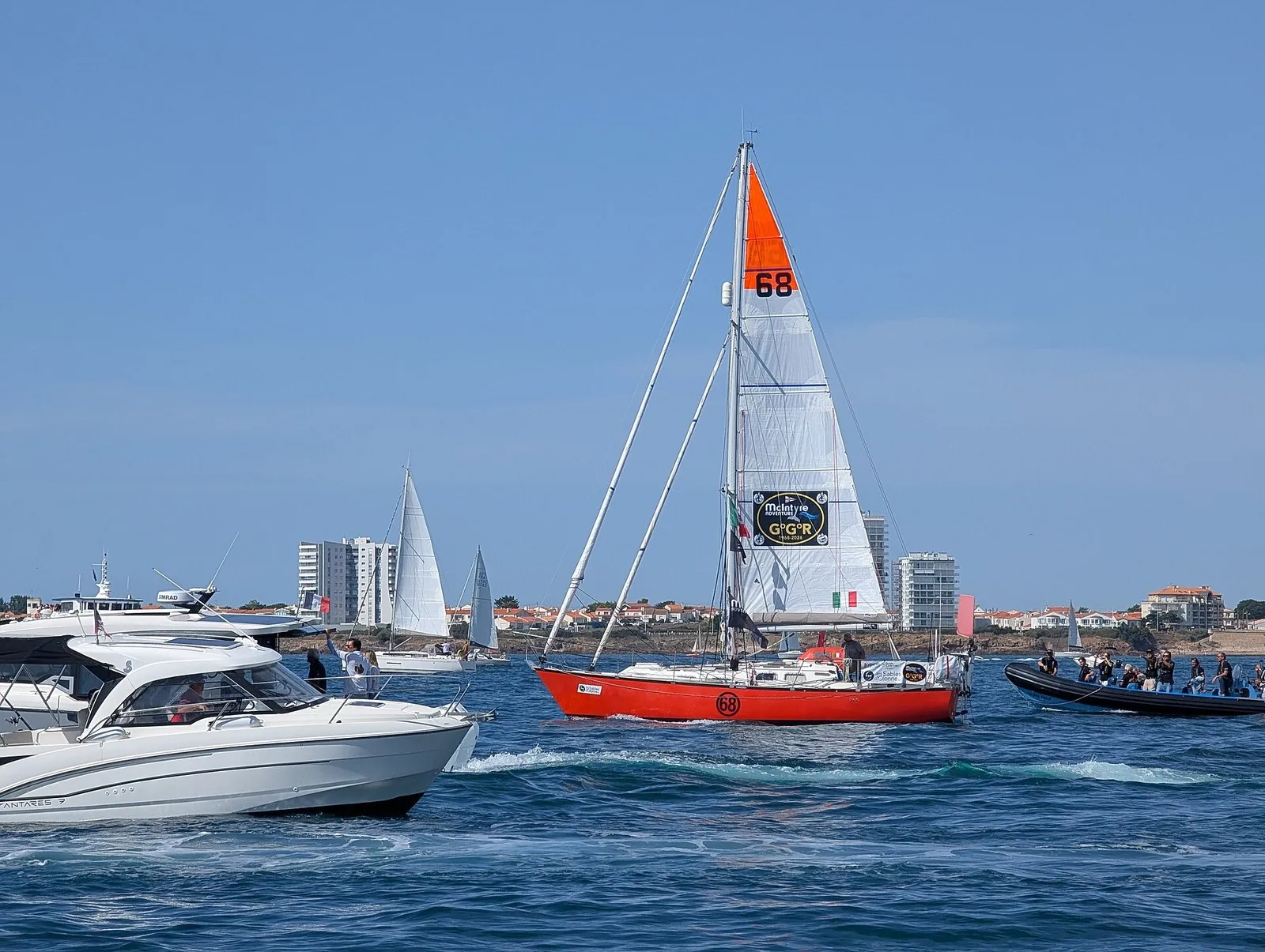 Яхта «Hanna of Cowes» в бухте Ле-Сабль-д'Олон на старте Golden Globe Race 2026, рядом катера зрителей