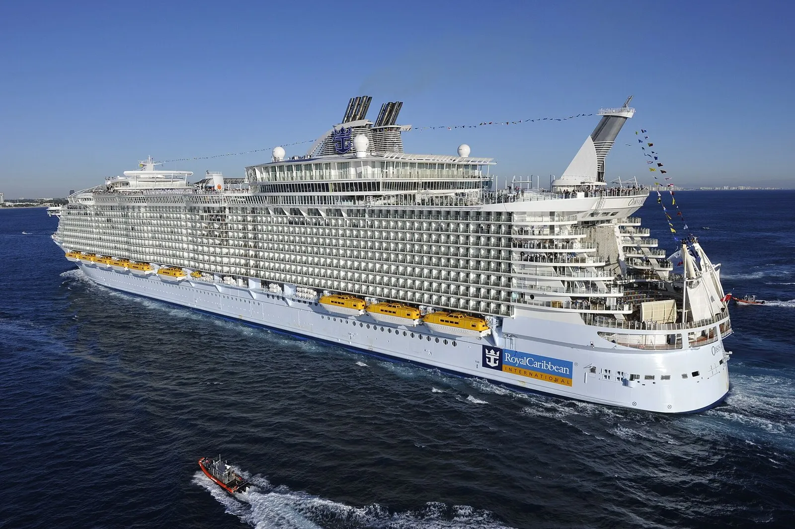 Oasis of the Seas на подходе к порту: ярусы палуб над белым корпусом, внизу небольшой катер сопровождения
