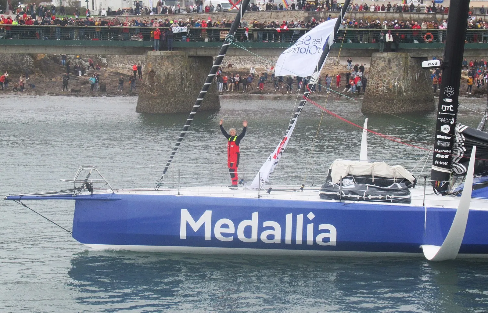 Яхта Medallia класса IMOCA 60 выходит на старт Vendée Globe 2024, справа у борта видна фольга