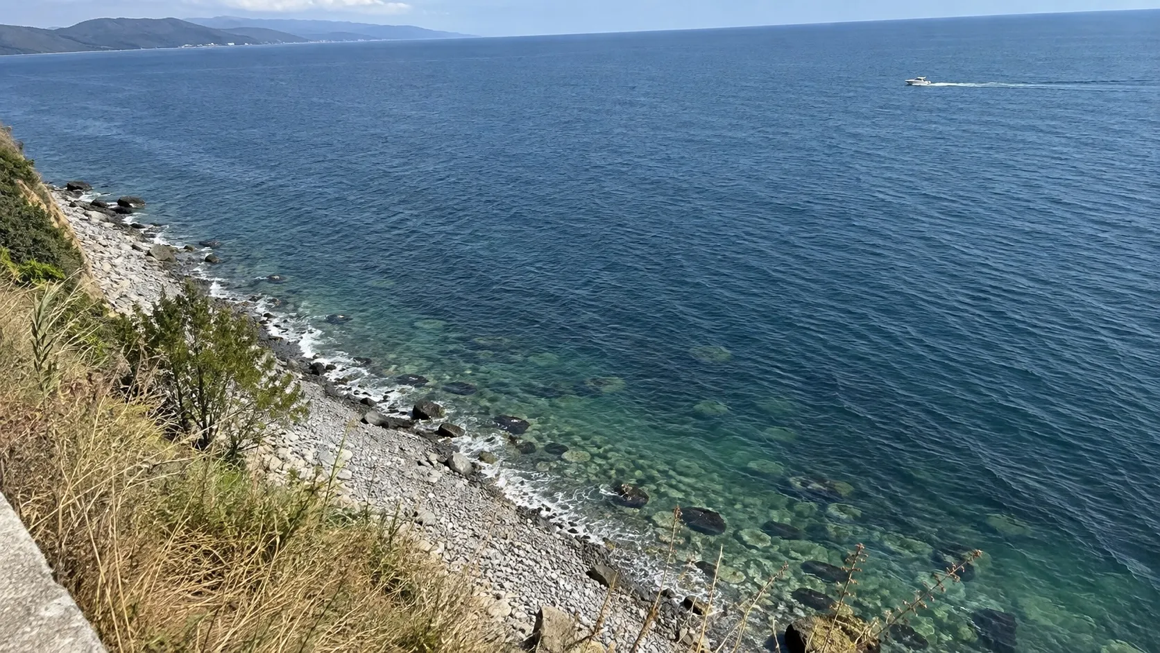 Зелёная полоса над камнем, за ней синяя вода и лодка мористее — черты на воде не видно, граница живёт только в координатах